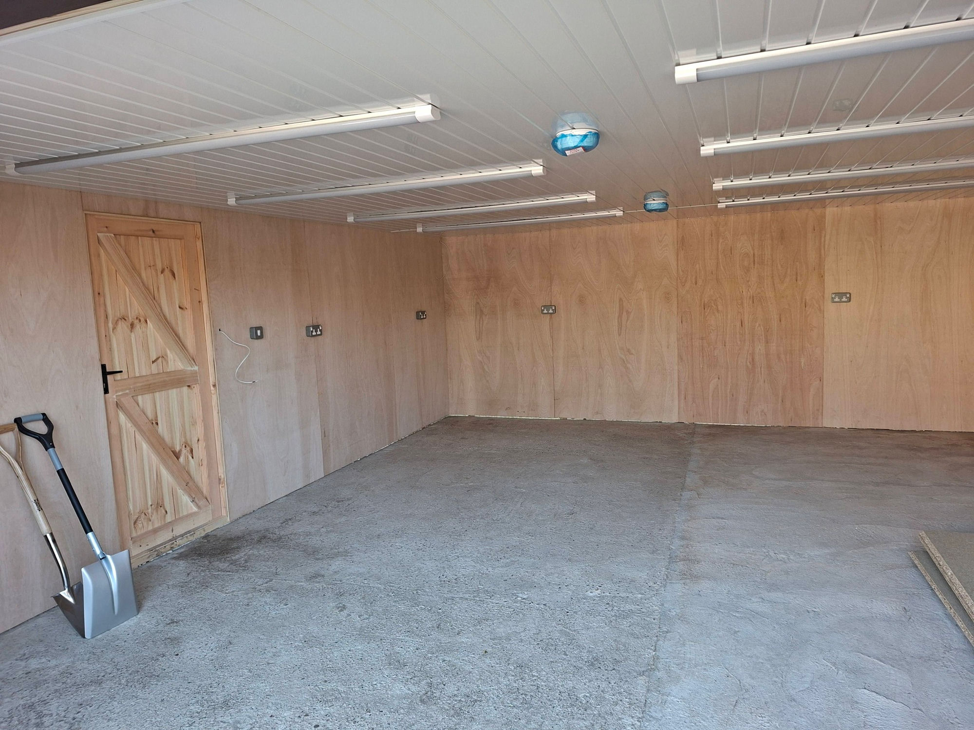 Garage conversion with plywood-lined walls, new lighting and power sockets